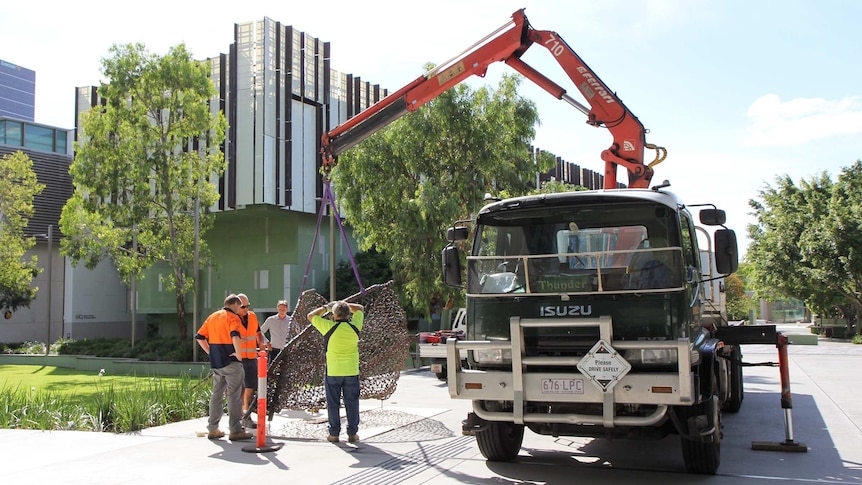 A crane lowers Judy Watson's sculpture, tow row, into position outside GOMA.