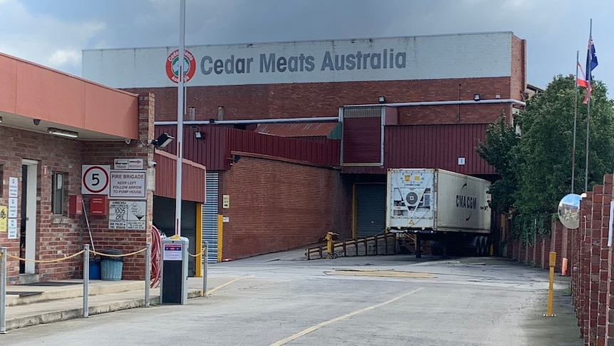 A truck is parked in an industrial driveway in front of a brick building marked 'Cedar Meats Australia'.
