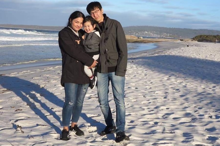 Two young Asian adults with a small child stand on a beach