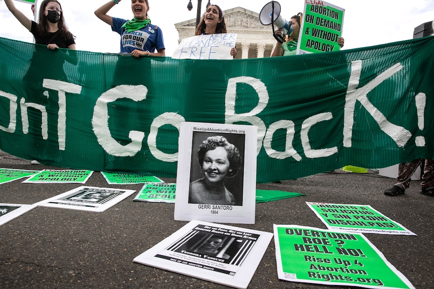 A photo of Gerri Santoro propped up before a protest banner reading "Won't Go Back!" 
