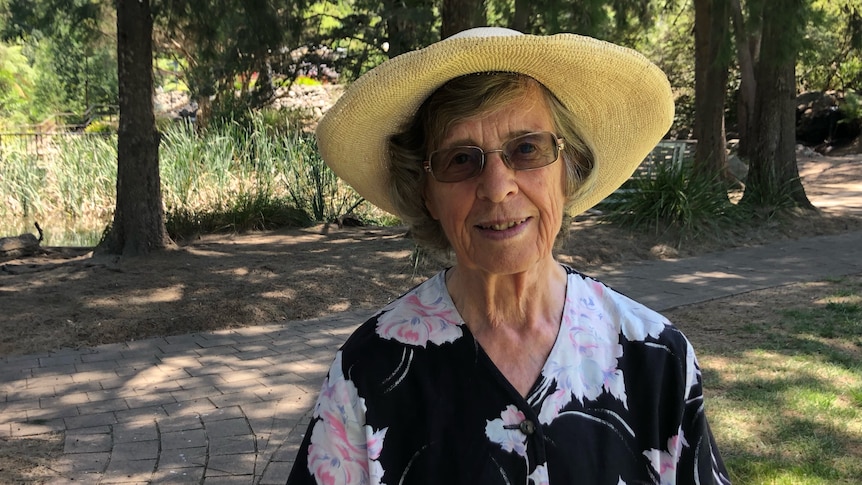 An older woman in a sun hat smiles.