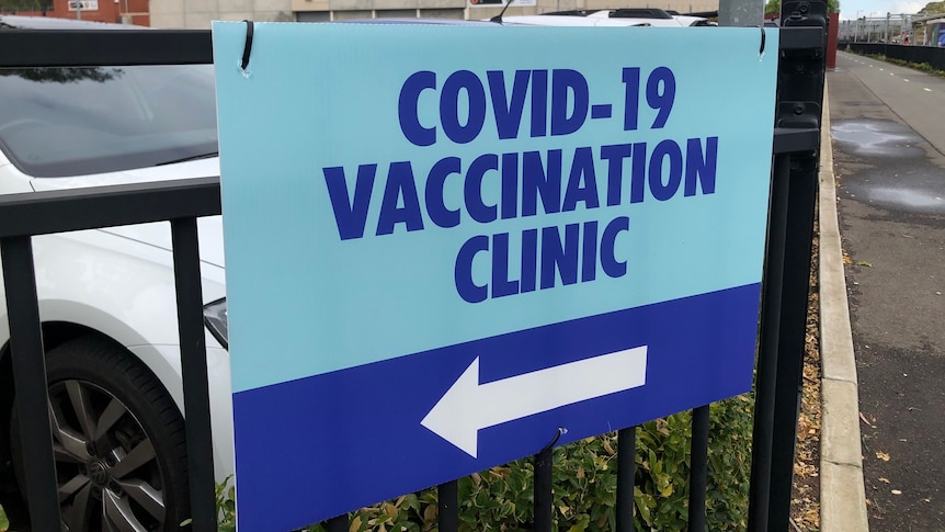 A sign on a fence saying COVID–19 vaccination clinic with an arrow to the left