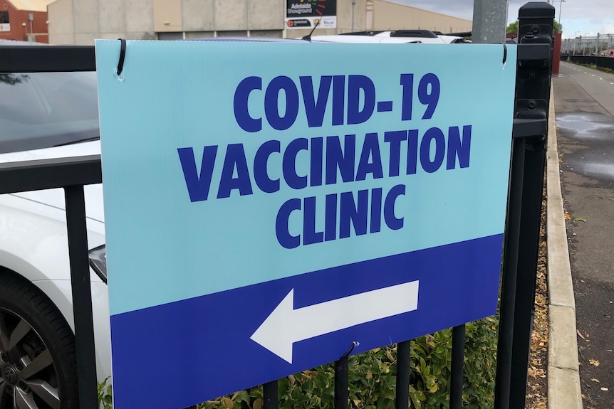 A sign on a fence saying COVID–19 vaccination clinic with an arrow to the left