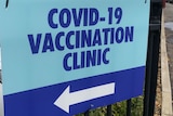 A sign on a fence saying COVID–19 vaccination clinic with an arrow to the left