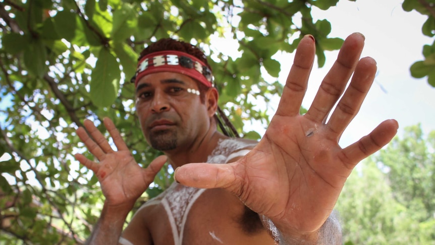 A photo of Weika in his Aboriginal paint posing in a traditional dance pose for the camera