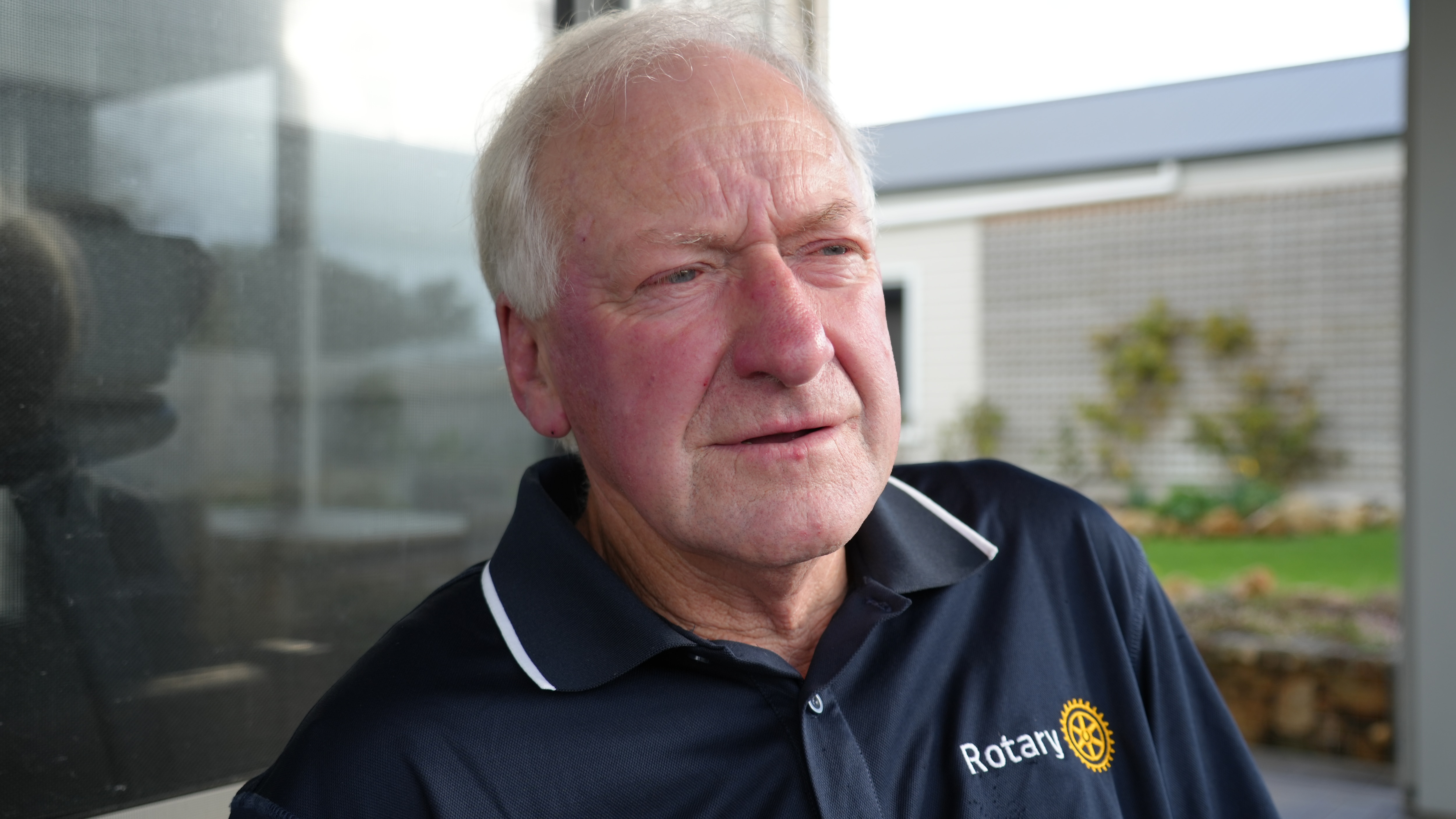 a man with white hair wearing a navy tee shirt looks away from the camera
