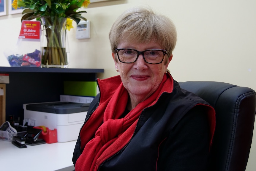 A middle-aged woman sitting at a reception desk smiles at the camera