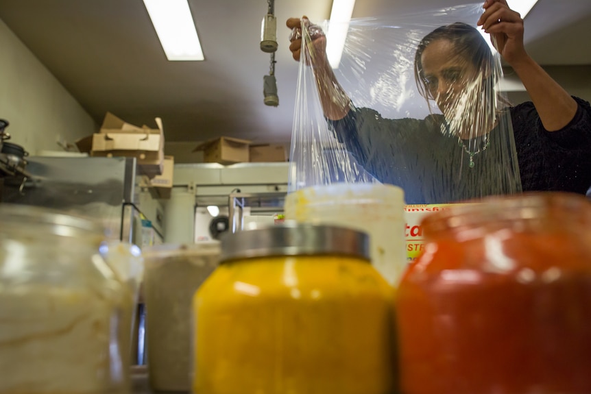 Ravit's face is seen through a strip of plastic wrap, jars of paprika and cumin in the foreground.