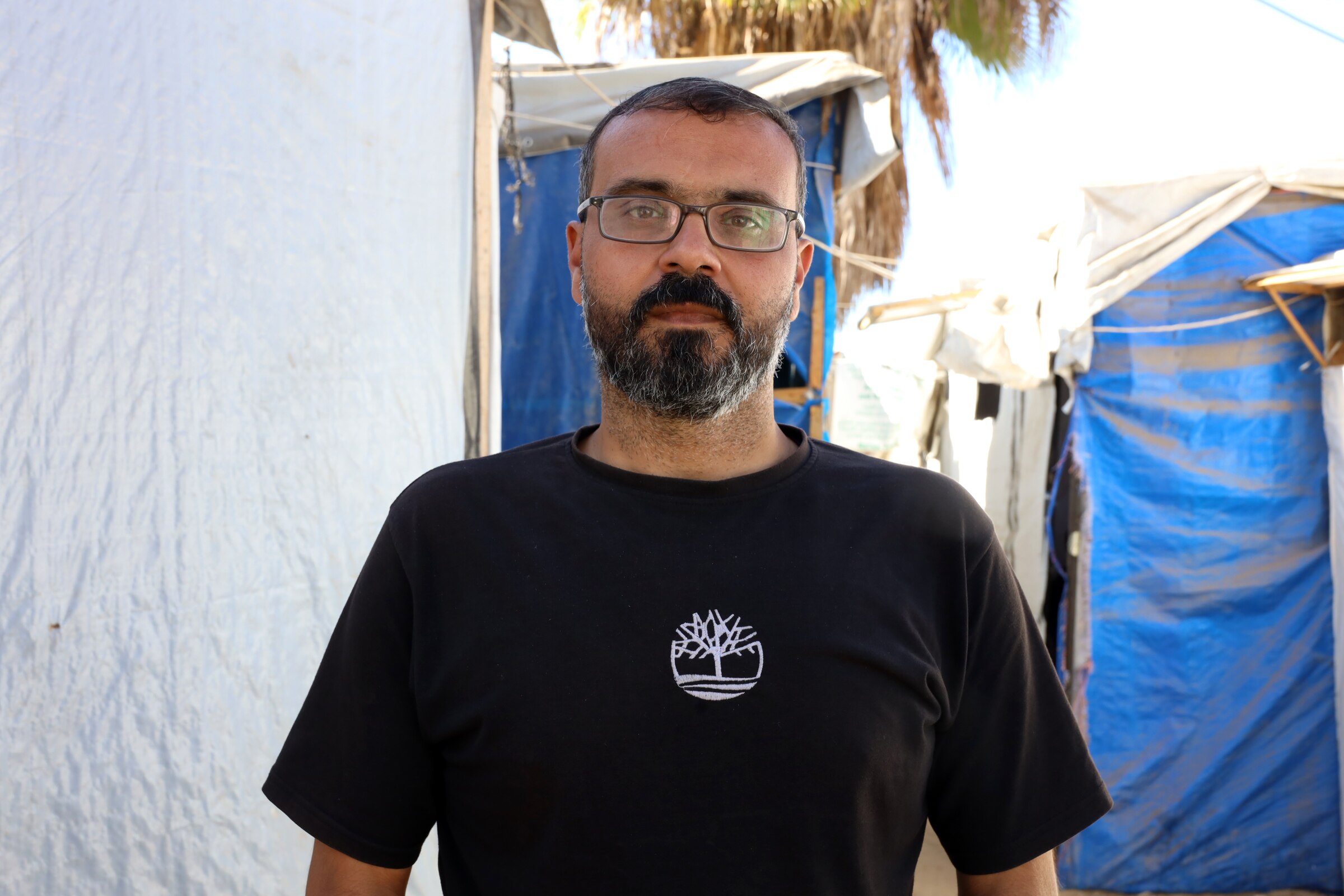 A man in a black shirt stands among tents.
