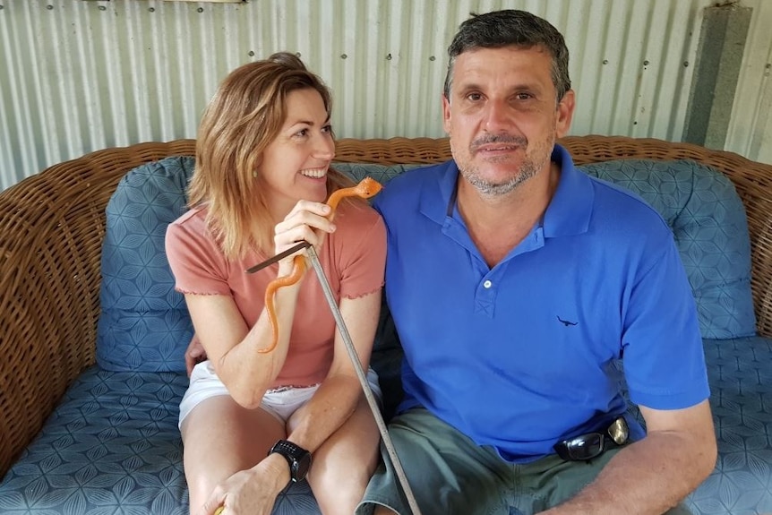 A smiling woman with light brown hair grins and wiggles a rubber snake at her husband.