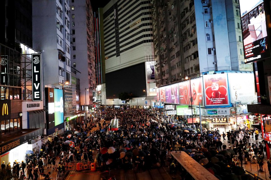 A huge group of people filling up a street in Hong Kong at night