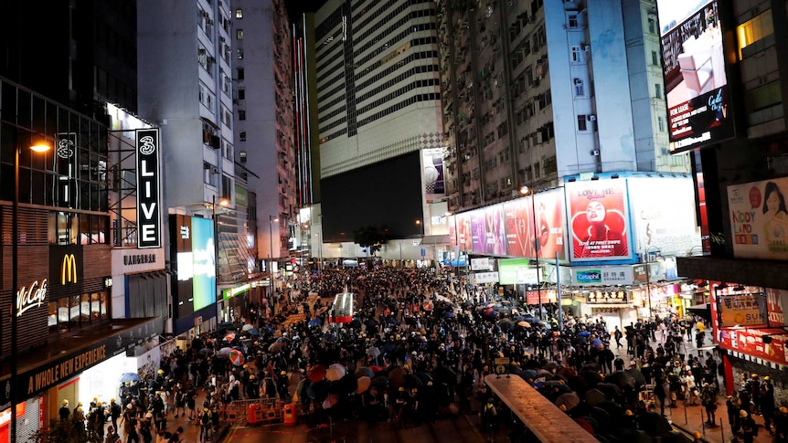 A huge group of people filling up a street in Hong Kong at night