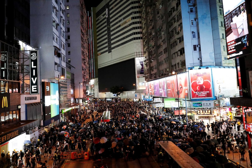 A huge group of people filling up a street in Hong Kong at night