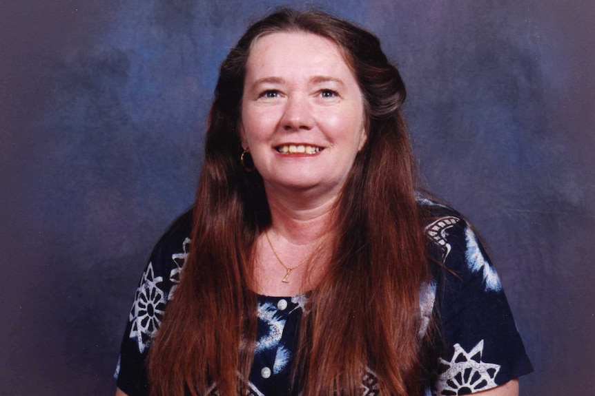 Portrait of a woman in her later forties smiling with long red hair.