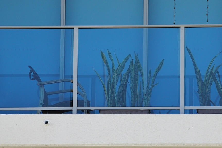 A close up of an apartment veranda, with a seat and pot plants.