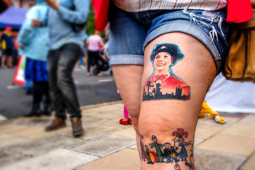 A close up on a woman's leg featuring a large tattoo of Mary Poppins on her thigh.