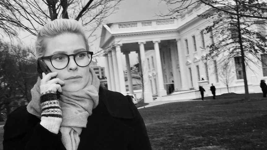 Black and white photo of Stephanie March on phone standing in front of the White House.