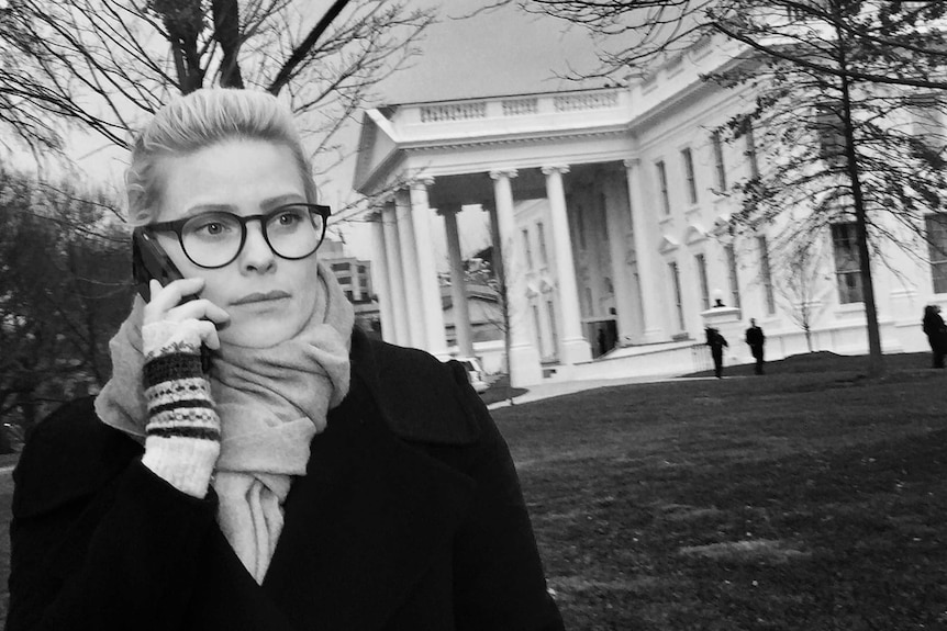 Black and white photo of Stephanie March on phone standing in front of the White House.