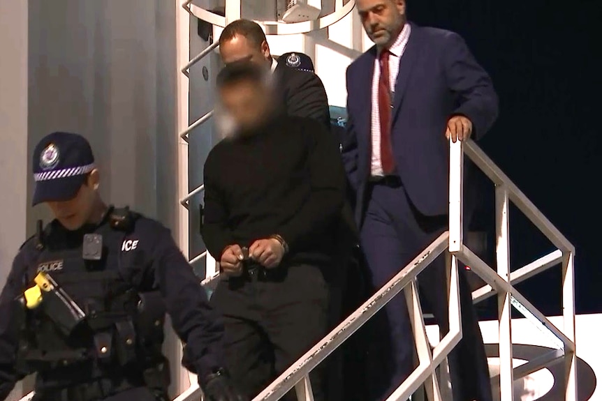 Several men, including one in handcuffs, walking down a set of outdoor stairs.