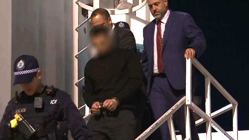 Several men, including one in handcuffs, walking down a set of outdoor stairs.