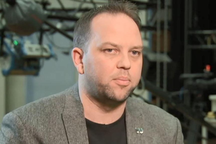 A man looking off camera with a TV studio in background.