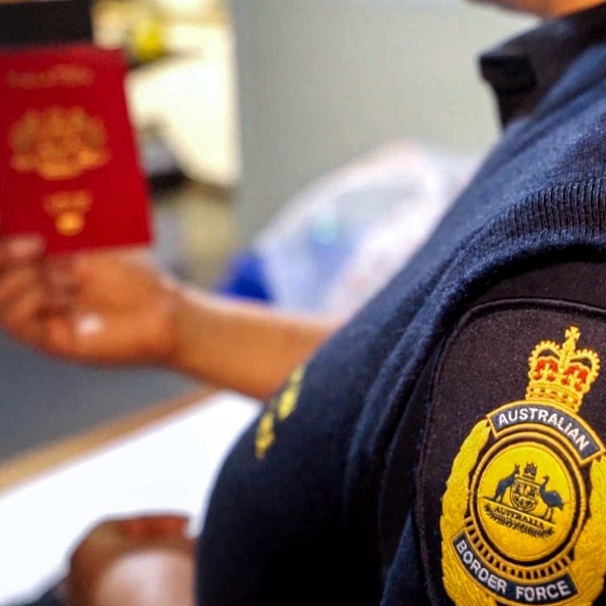 An Australian Border Force officer, with badge in foreground, holds a passport in background.