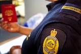 An Australian Border Force officer, with badge in foreground, holds a passport in background.