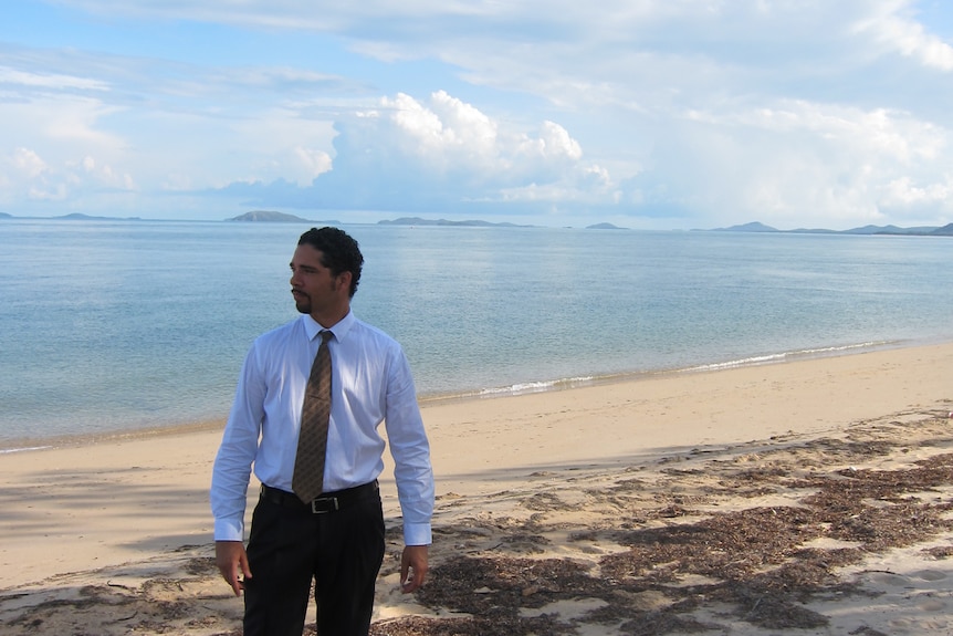 Man dressed in suit pants and shirt stands on a beach.