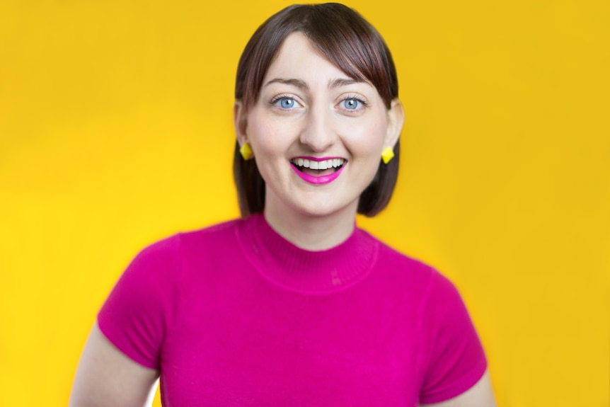 A headshot of a woman in a pink top in front of a bright yellow background.