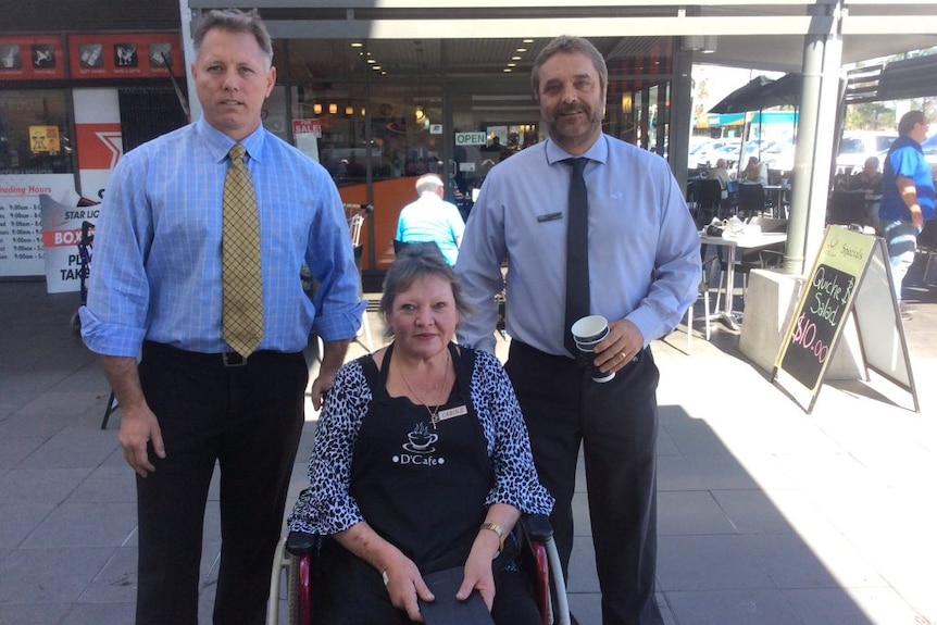 A man, a woman in a wheelchair and and man standing outside a cafe