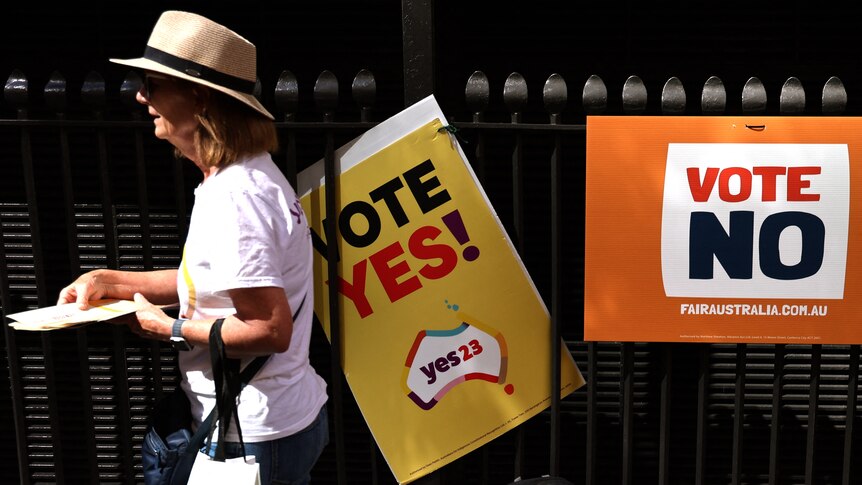 A woman walks past "vote yes" and "vote no" signs on a fence. 