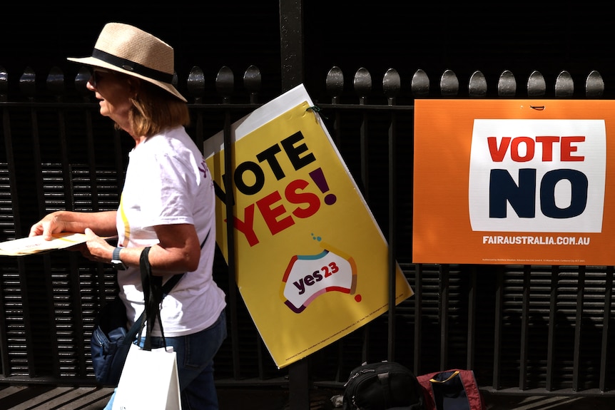 A woman walks past "vote yes" and "vote no" signs on a fence. 