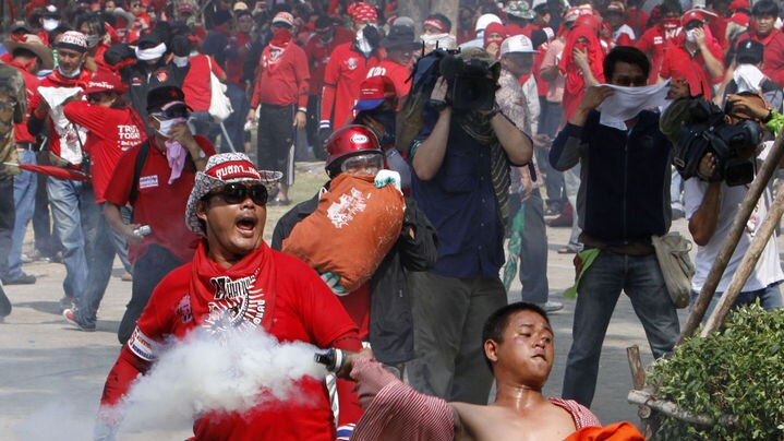 An anti-government red shirt protester throws a tear gas canister back at army soldiers in Bangkok,