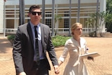 A man, Lane Muller, is seen walking in front of the NT Supreme Court building, holding hands with a woman.