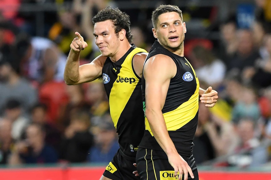 A Richmond AFL player smiles and points a finger as he embraces a teammate while celebrating a goal against St Kilda.