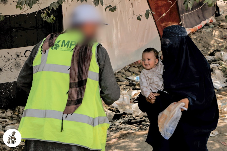 A man in a high viz jacket hands something to a woman and her baby