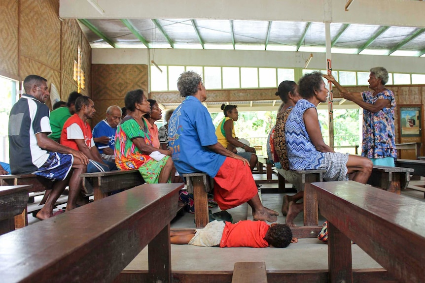 A boy lies on the ground as the adults around him, sitting in church pews, sing in a choir.