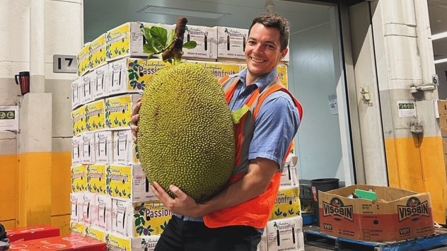 A man is smiling at the camera holding an oversized jackfruit.