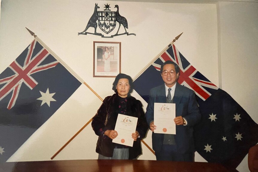 Two well dressed Asian people stand in front of Australian flags.