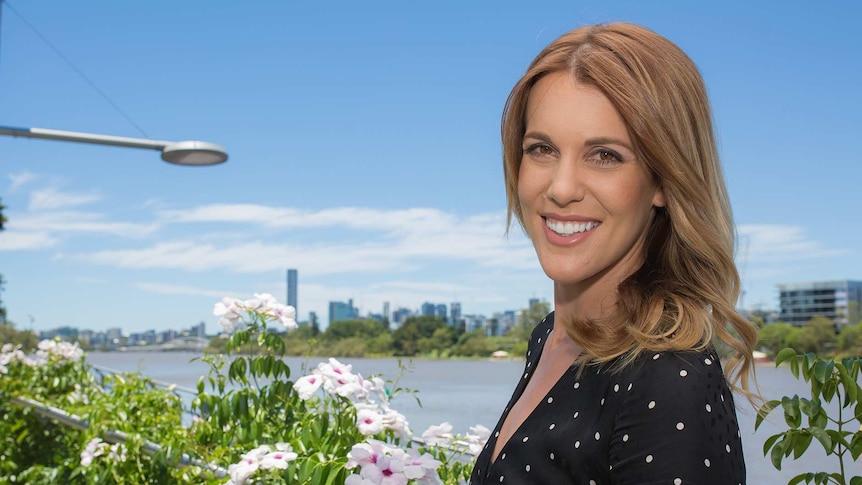 A woman with dark blonde, shoulder-length hair standing near the Brisbane River.