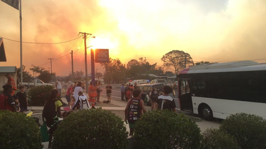 Residents standing at the police station with huge plumes of smoke in the background.