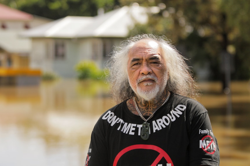 A man stands in front of a flooded house.