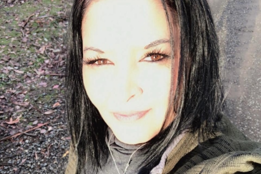 A woman with dark hair takes a selfie, smiling at the camera.
