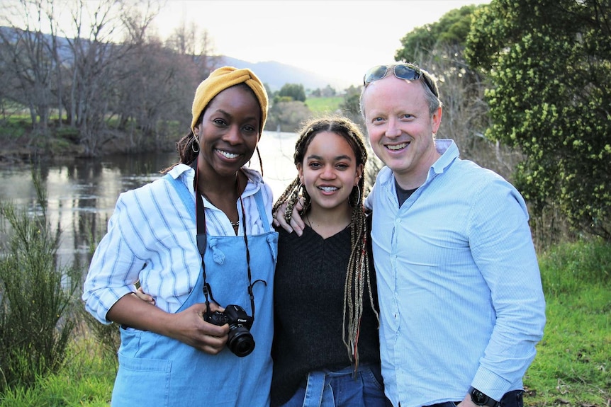 Melanie McCollin-Walker with her husband Brent Walker and daughter Aaliyah stand on the bank of a river.