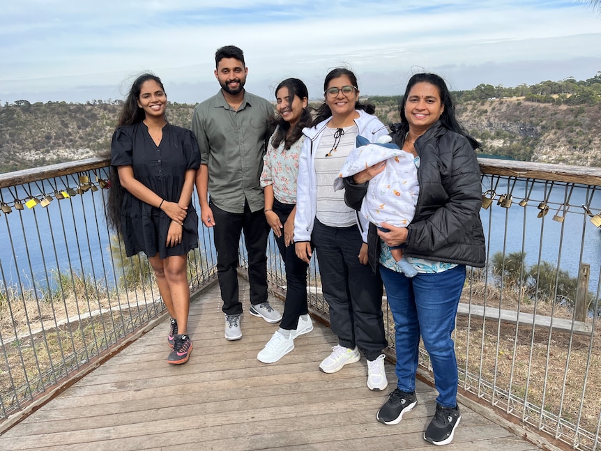 Four women, a man and a baby at a lookout over a lake.