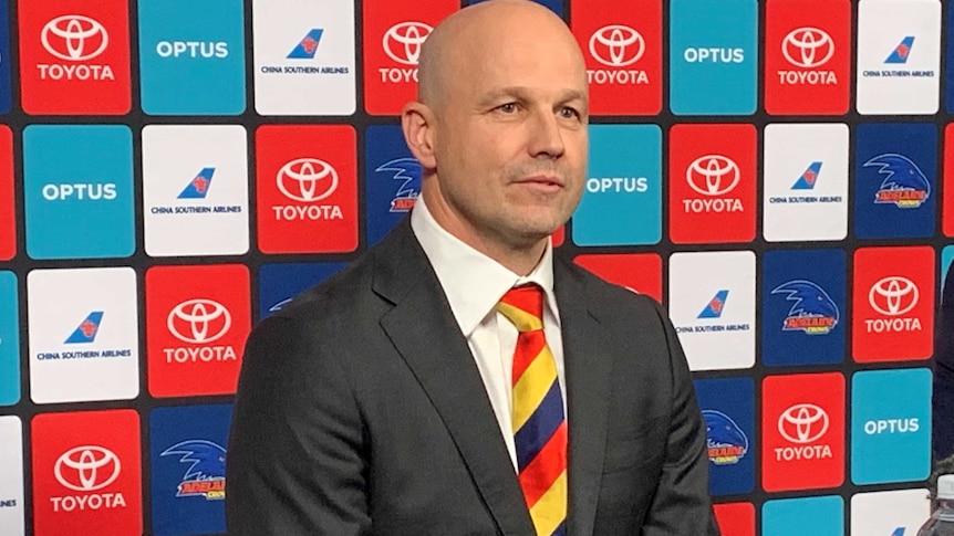 Matthew Nicks sits down wearing a black suit and yellow, blue and red tie