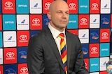 Matthew Nicks sits down wearing a black suit and yellow, blue and red tie