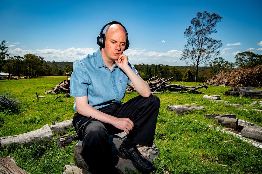 A man looking pensive in a field wearing noise cancelling headphones