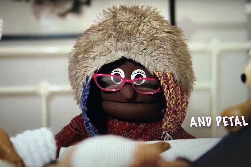 Puppet, in glasses and wearing a beanie, stares at the camera