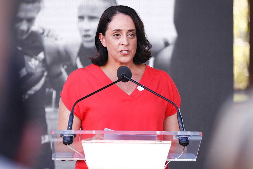 Wearing red, she stands in front of a microphone.